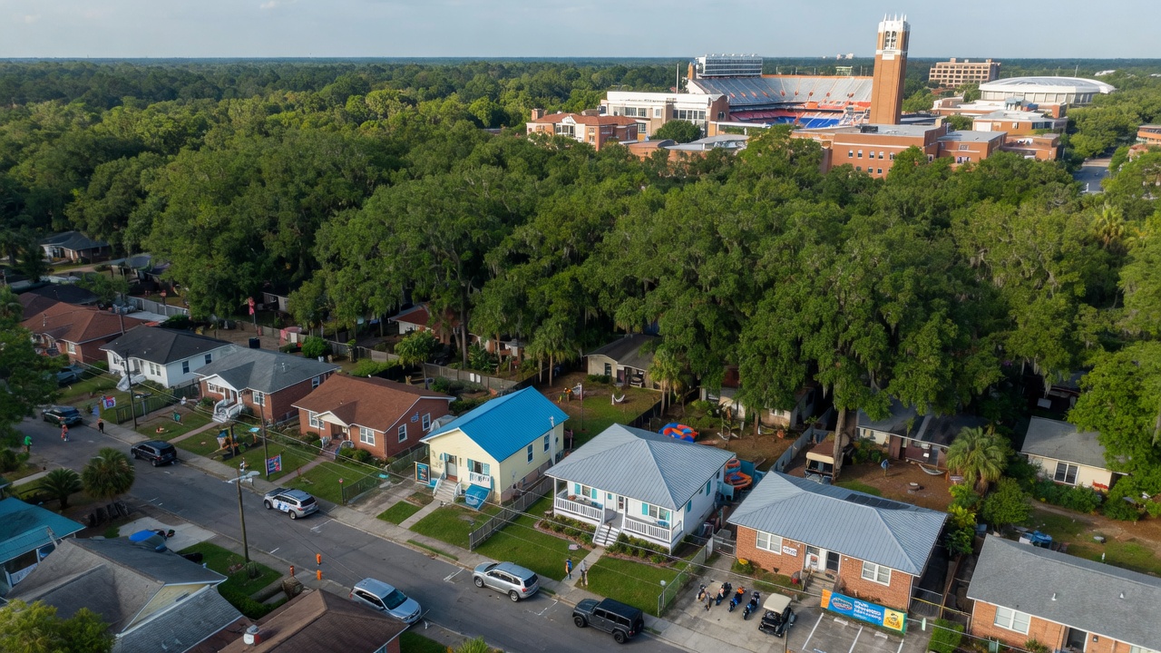Professional 8K aerial view of Gainesville Florida neighborhood near University of Florida showing mix of single family homes suitable for short-term rentals, beautiful tree canopy, campus visible in distance