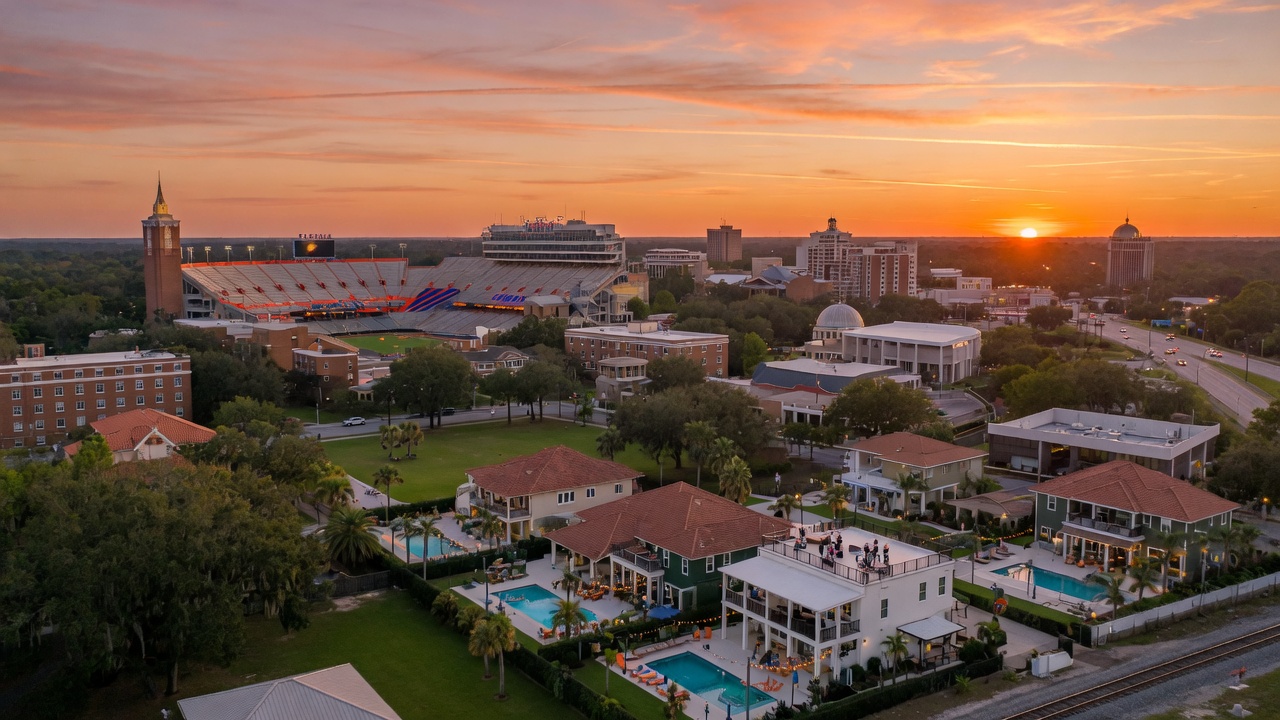 Ultra-realistic 8K aerial view of Gainesville Florida skyline at sunset with University of Florida campus visible in background, Ben Hill Griffin Stadium prominent, warm golden hour lighting, luxurious Airbnb properties in foreground, cinematic composition